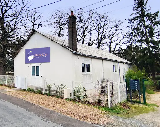 Vue extérieur de la pension avec son enseigne rectangulaire. Des arbres en arrière plan du bâtiment.